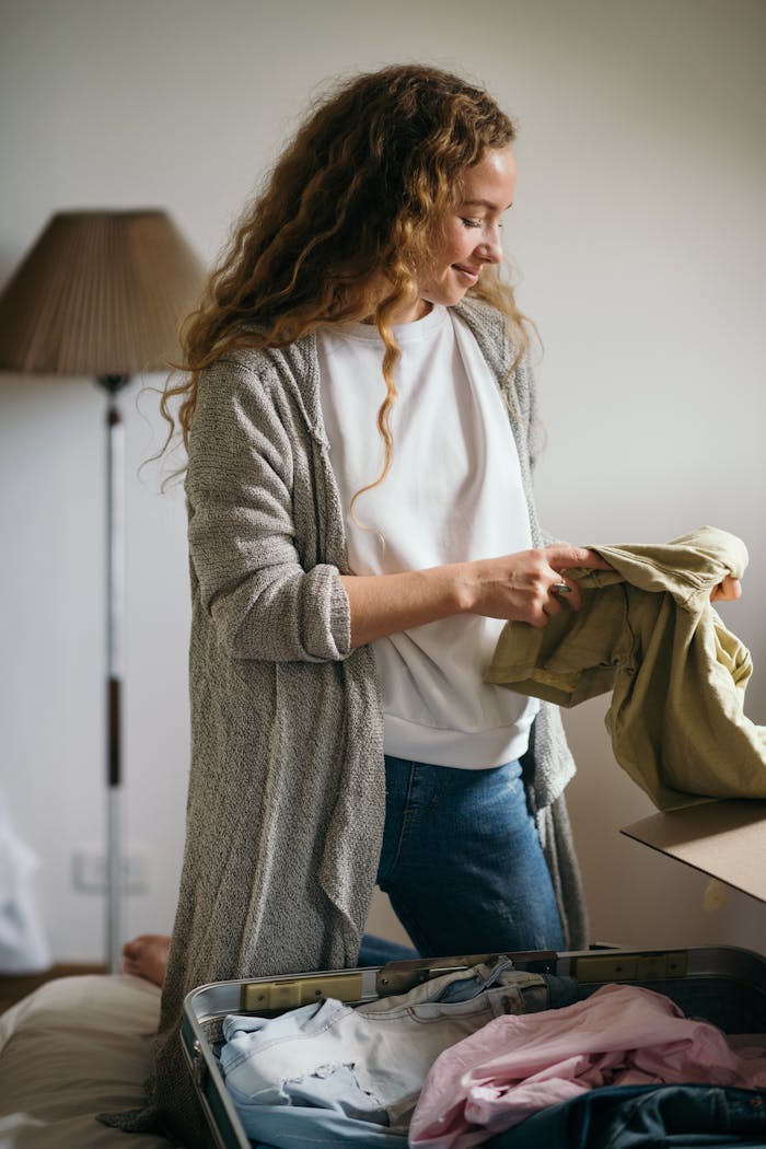 Smiling woman packing suitcase in modern bedroom, preparing for a trip.